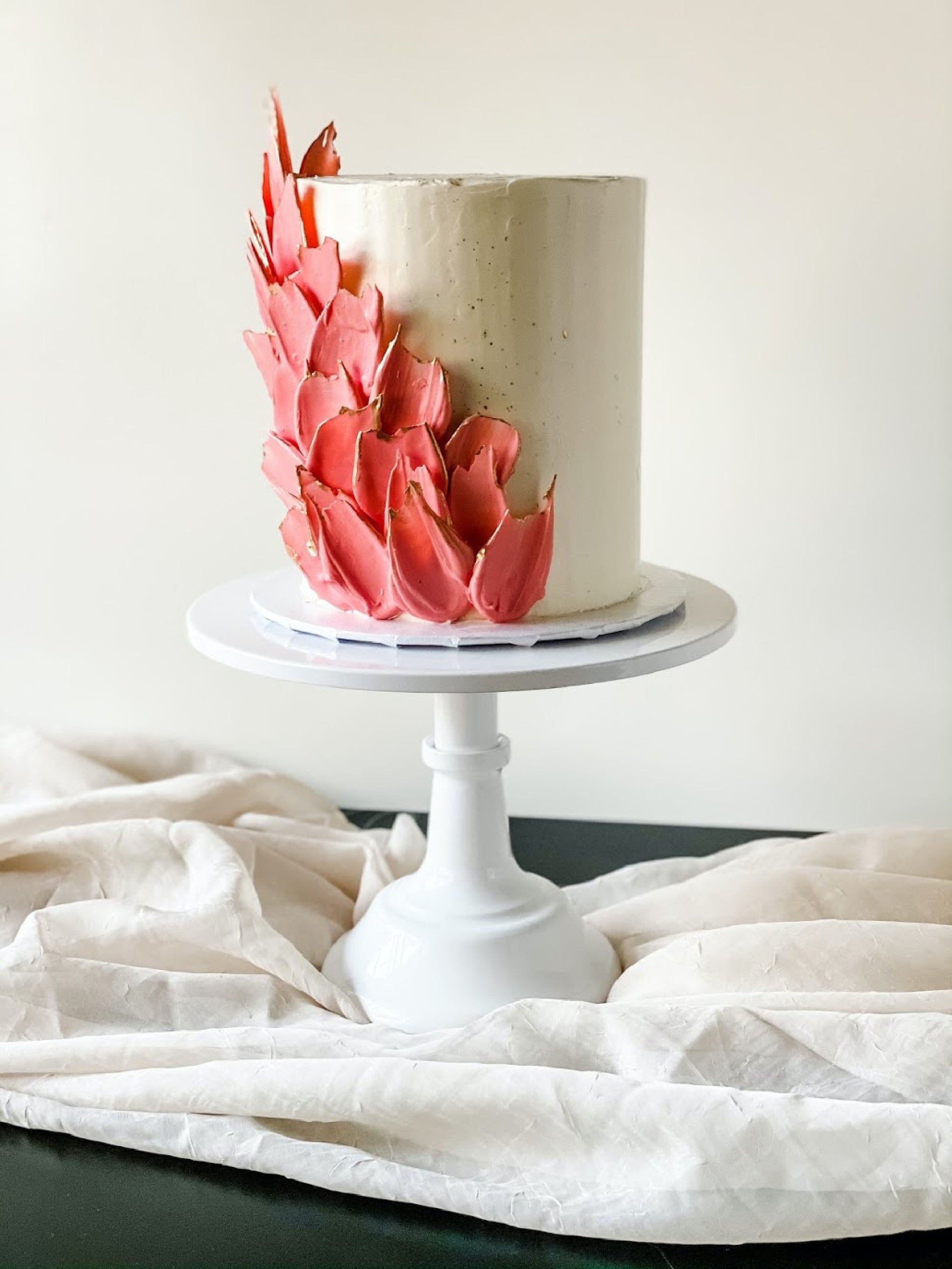 a tall vanilla cake made with Adri Wellness' Hibiscus powder frosting on a cake stand