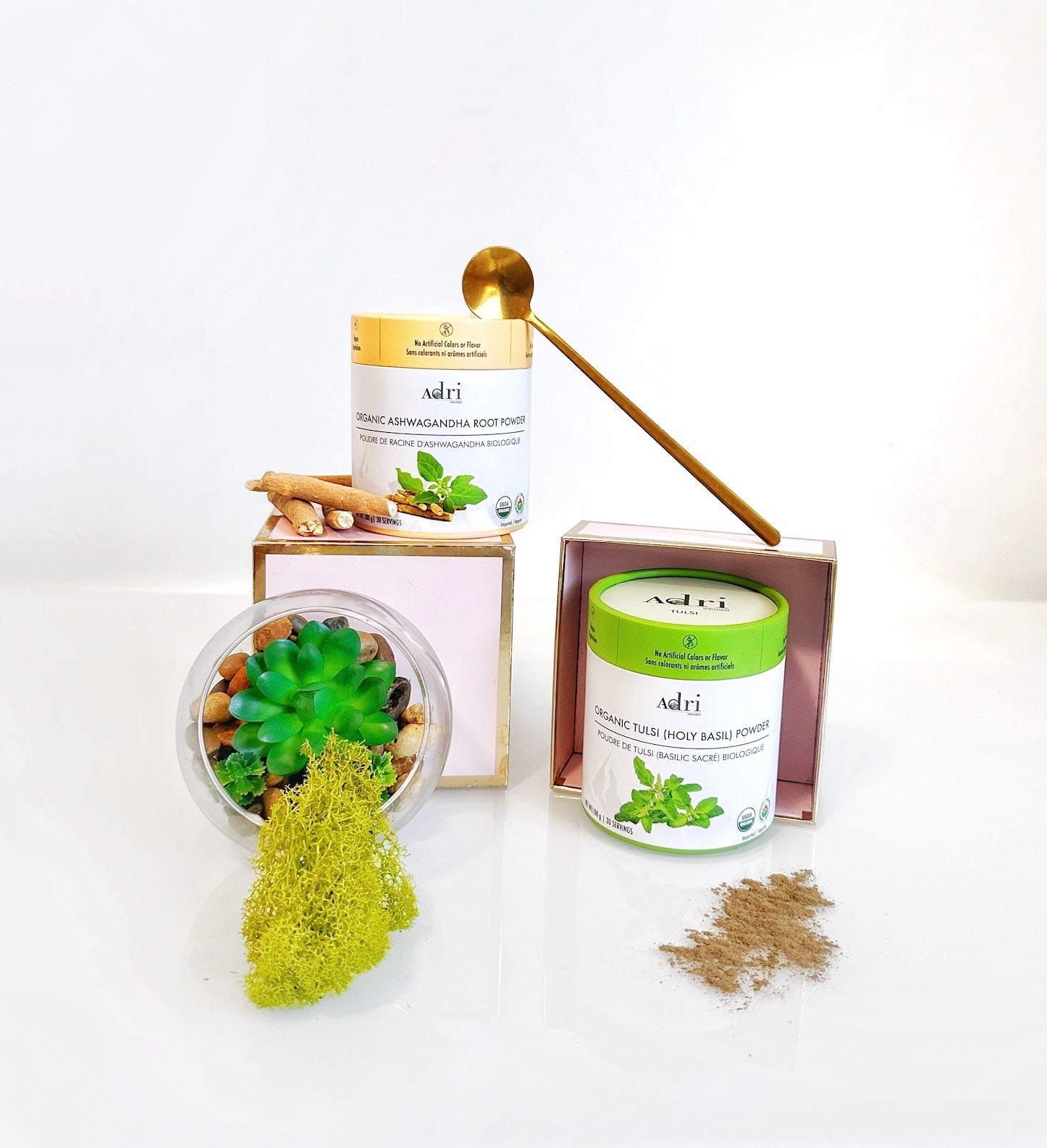 Adri Wellness Ashwagandha and Tulsi powder showcased together with a golden spoon, raw ashwagandha root, andfaux grass