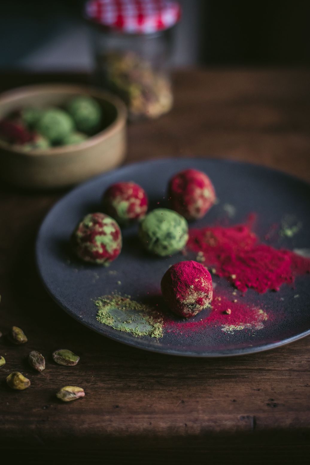 Energy balls made with pistachio powder and Adri Wellness' Beetroot powder placed on a black plate with scattered beetroot powder