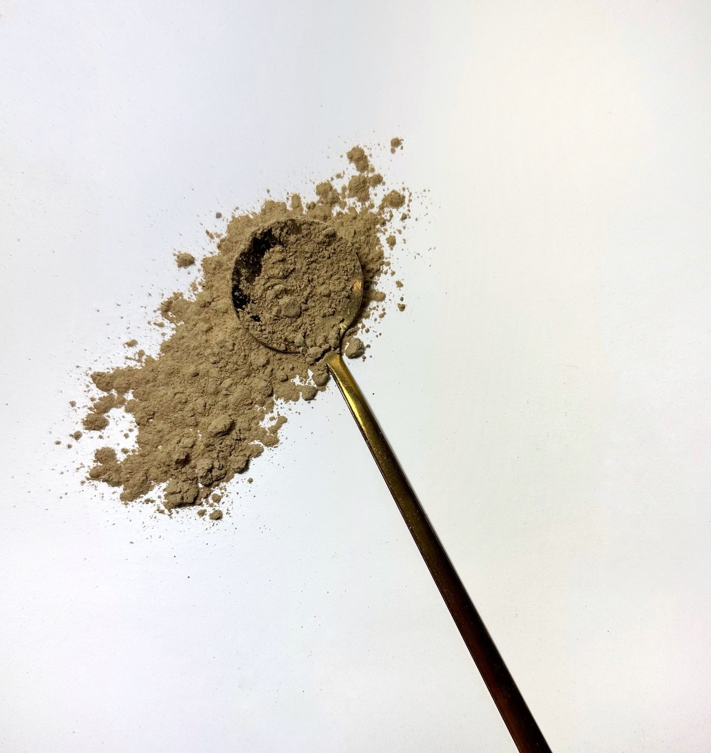 Adri Wellness's fine organic Triphala powder scattered on a white surface with a golden spoon
