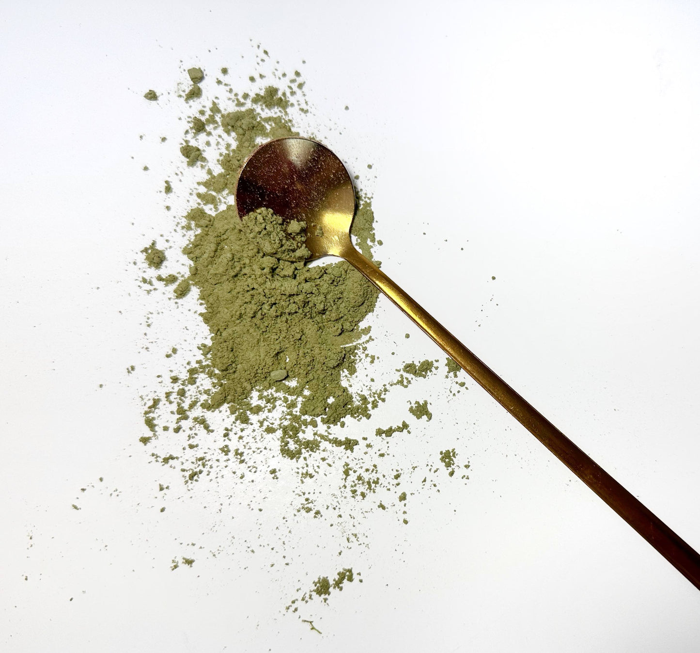 Adri Wellness's fine organic Wheatgrass powder scattered on a white surface with a golden spoon