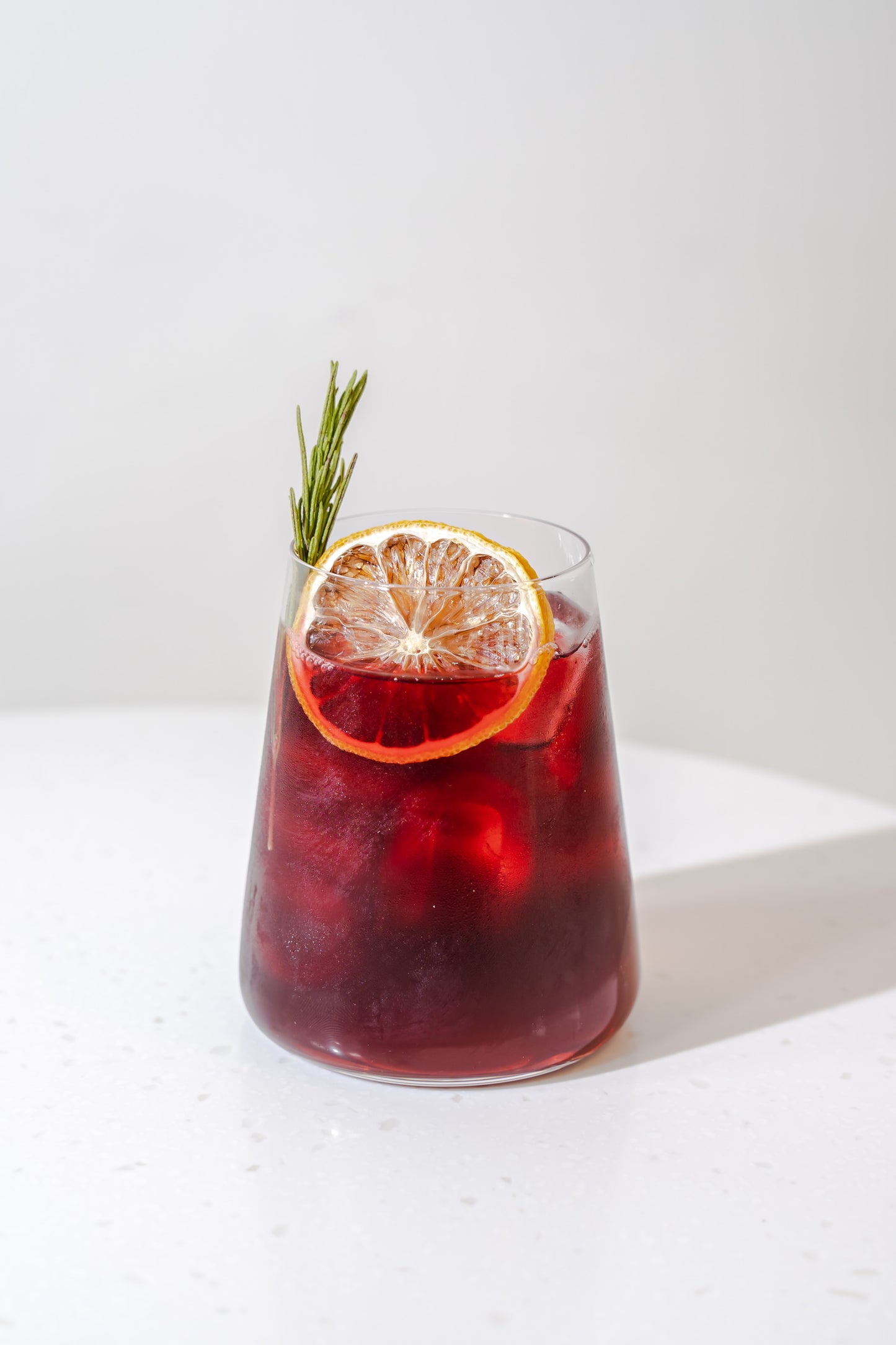 a transperant glass of an icy mocktail made with Adri Wellness' Hibiscus powder garnished with a piece of lemon