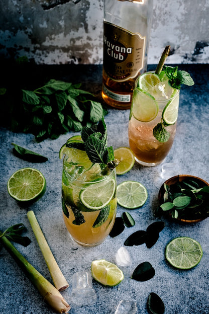 a tall glass of an icy drink made with fresh mint, lime, soda and Adri Wellness' lemongrass powder placed on a darker surface