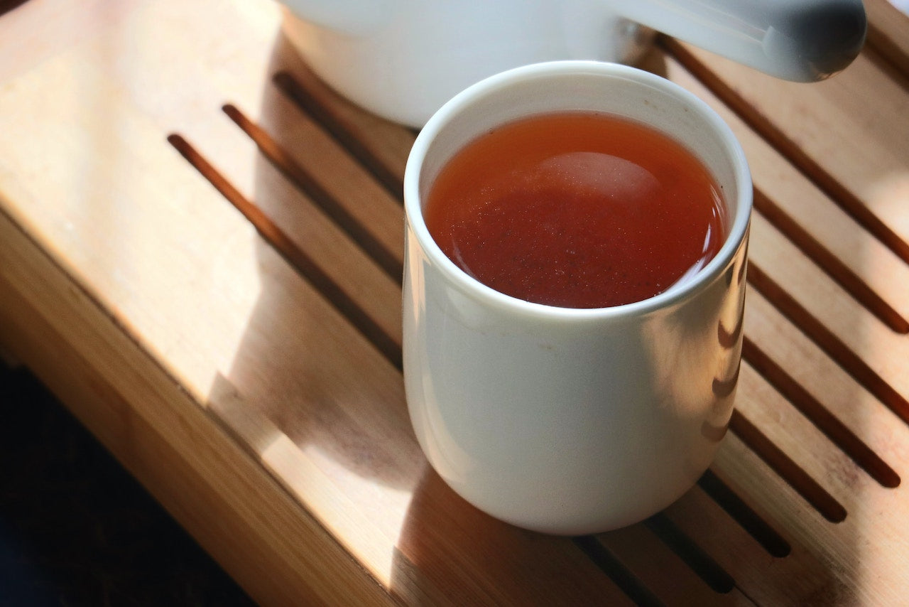 a warm white cup of tea made from Adri Wellness' Manjistha powder placed on a wooden platform