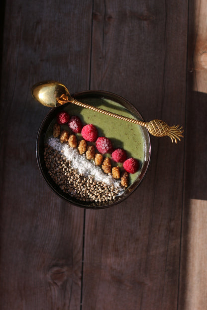 a green smoothie bowl made with Adri Wellness' Moringa powder garnished with raspberries, seeds and desiccated coconut including a golden spoon